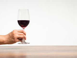 Hand holding a glass of red wine against a gray background.