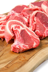 Stack of fresh lamb loin chops on wooden cutting board and on white surface. Premium high quality red meat. Butcher craft. Uncooked product.