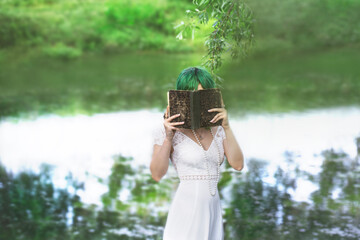 mysterious girl hides her identity behind a book in the middle of a green nature