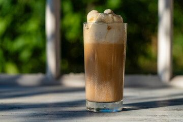 Glass of coffee with ice cream on the windowsill next to the window. Cold summer drink. Closeup