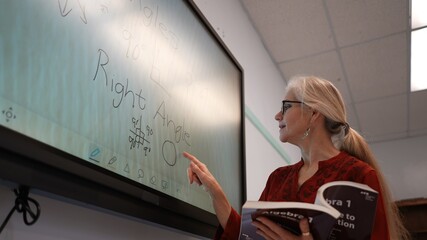 Closeup of happy female teacher writing on an interactive whiteboard teaching geometry math in a...
