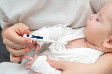 Mother uses electronic thermometer on sleeping newborn, Concept of baby's high temperature
