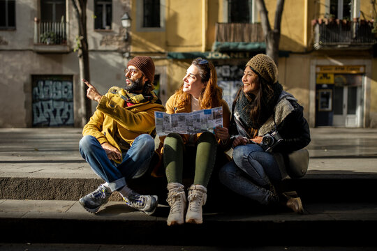 Group of tourists looking a map walking on the street. Three cheerful friends seraching a monument during a city travel