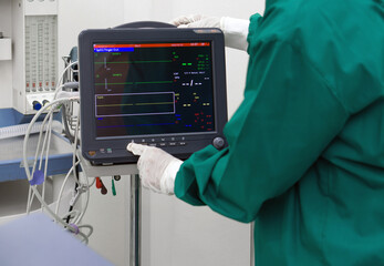 Multi-parameter patient monitor in operating room, controlled by nurse in surgical green gown...