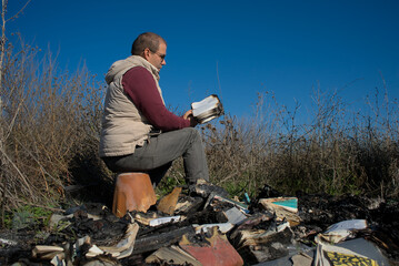 A man sits on the ashes among burnt books and reads a book preserved from the fire.