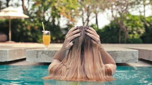 Back view of woman emerging from under water while being in swimming pool on tropical vacationBack view of woman emerging from under water while being in swimming pool on tropical vacationBack view of