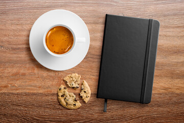 Top view of a blank hardcover leather notebook on a wood office desk table with a cup of coffee and a chocolate cookie. High resolution.