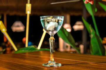 Restaurant and bar concept. Table with a tall, elegant spirit glass filled with blue drink and ice, exuding a chic and luxurious atmosphere. Selective focus. 