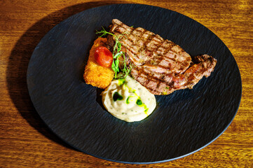 On a black plate, a serving of pan-seared meat accompanied by a side of garnish. Close up photo. Restaurant and bar concept. Selective focus.