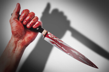 Male hand with a knife in blood stains casting shadow on white background