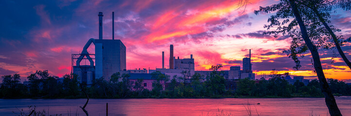 Fototapeta na wymiar Dramatic sunset cloudscape over the Penobscot River in Bradley, north of Bangor, Maine, with the views of old factories and slanted trees in silhouette