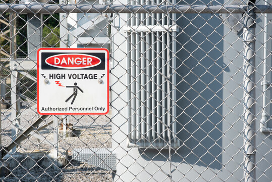 Danger high voltage, authorized personnel only sign on a chain linked fence surrounding an electrical switch yard.