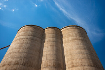 Three grain silos, looking up, with a strong perspecctive, against  a blue sky with wispy clouds