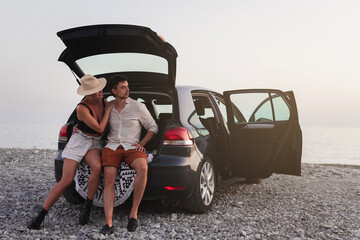 Couple of travelers standing beside their car on a pebble beach during their road trip