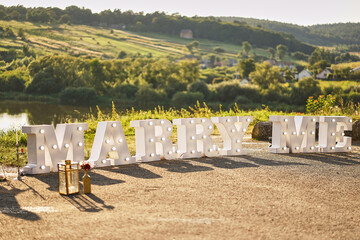 The inscription "marry me" glows on the lawn near the lake