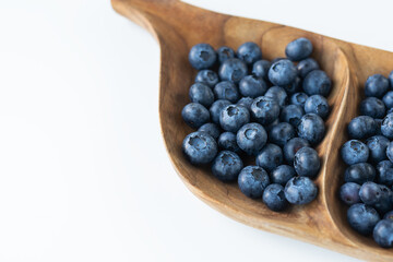 Ripe blueberries in a wooden interesting plate close-up on a white background. Delicious and healthy berry. Place for an inscription.
