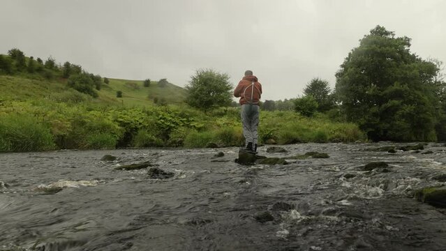 Hand-held shot of a fly fisherman standing on a rock casting into a quick river
