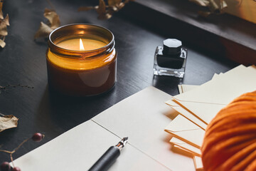 Cozy autumn still life with pumpkin, sheets of paper, fountain pen and burning candle on the...