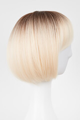 Fototapeta premium Natural looking blonde fair wig on white mannequin head. Short hair cut on the plastic wig holder isolated on white background, side view.