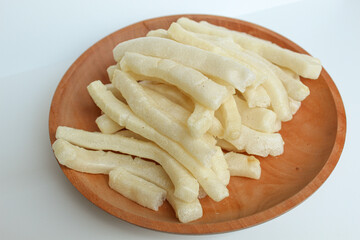 Kerupuk panjang, Indonesian snack or food condiment. Fried tapioca flour in long thin shape. On wooden plate, isolated on white background