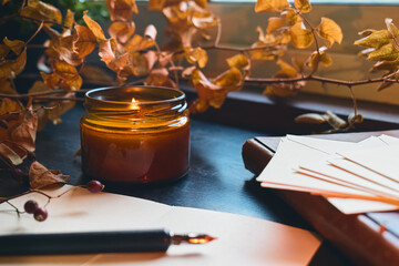 Cozy autumn still life fall leaves, sheets of paper, fountain pen and burning candle on the...