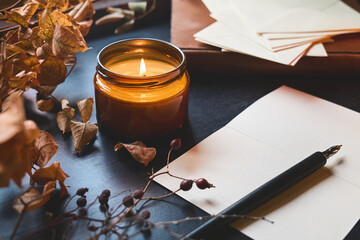 Cozy autumn still life with pumpkin, sheets of paper, fountain pen and burning candle on the...