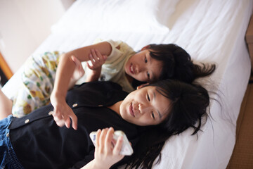 ホテルの客室のベッドでスマホを見ている子供姉妹の笑顔