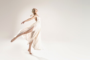 Fototapeta na wymiar Ballerina in maxi dress dancing over light studio background. Ballet Dancer. Modern Dance. Graceful Woman. Hobby.