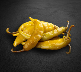Pickled hot green peppers, tzitzak, handmade pickles on a dark stone background.