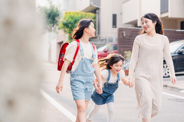 お母さんと手を繋いで学校に行く2人の女の子