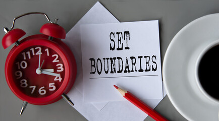 SET BOUNDARIES - words on white paper on the background of an alarm clock, a pencil and a cup of...