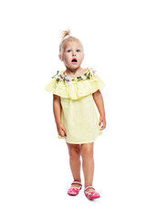 Surprised little girl 2 years old in a yellow dress stands with her mouth open. Full height. Isolated on white background. Vertical.