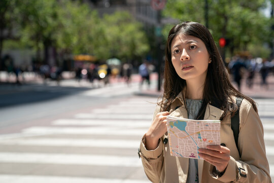 asian taiwanese girl tourist looking into distance to check directions with city map in hand near crosswalk while touring around downtown san Francisco in California usa