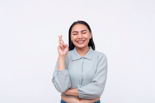 A young asian woman closes her eye wishing for good luck. Crossing her fingers hoping for the best. Isolated on a white background.