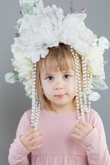 Little girl wearing white flower hat looking at camera on gray background