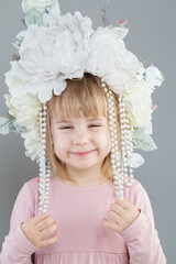 Pretty kid girl in white flower hat smiling on grey background