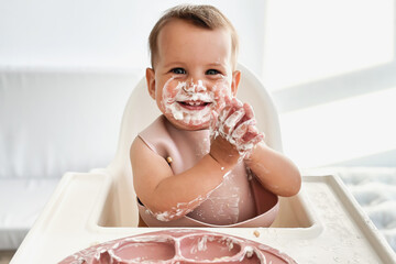 cute beautiful baby infant girl eats cottage cheese and smiles, looks at the camera, grimy and...