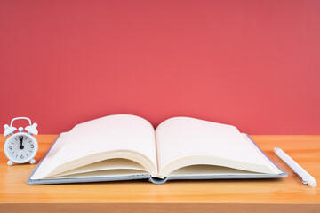 The Open blank notebook and pen with alarm clock on the table.