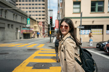 smiling asian korean business lady wearing sunglasses turning to look at camera while waiting to cross the street near chinatown in san Francisco California usa on windy day