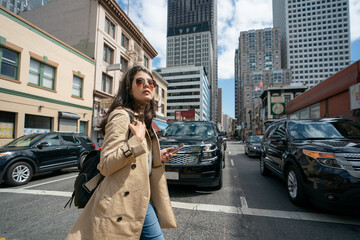 fashionable asian Taiwanese woman tourist passing by cars as she's crossing the road during her visit in downtown san Francisco California usa. she looks into distance while walking