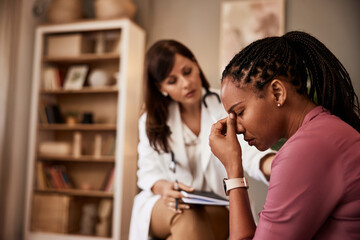 An African-American woman struggling with deep depression and talking with a female doctor.