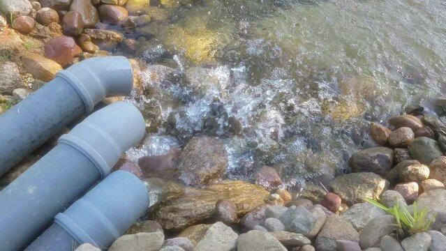 Fresh drinking water from the artesian well comes through a water pipe. A stream of sewage flows out of a plastic sewer pipe into the river.