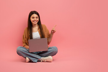 Check This. Teen girl sitting on floor with laptop and pointing aside