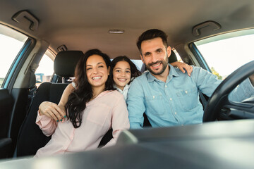 Happy european family with child girl sitting inside car and smiling at camera, enjoying road trip...