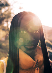Close-up outdoor shot of a beautiful young and proud African woman model with pigtails and dark hair looking at the camera against sunlight backlight
