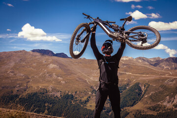 Biker with a bicycle in his hands above his head. Electric bike in the mountains.