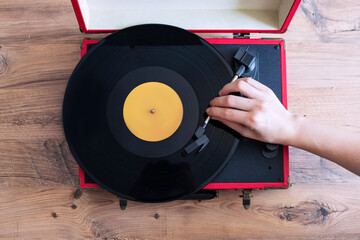 Female hands set up retro vinyl record player with plate on wooden table. Top view