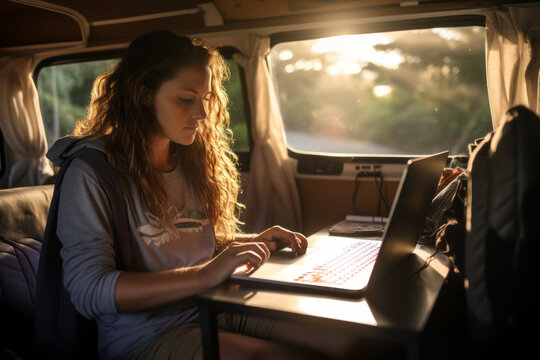 Beautiful young digital nomad using a laptop computer in camper van on sunny day. Woman working remotely with her laptop. Digital nomadic life.