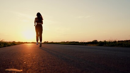 Running after sun. Training jogging. Beautiful girl doing fitness, jogging on road in sun. Jogger...
