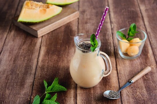 Melon smoothie with chia seeds in a serving jug on a brown wooden background. Melon recipes. Refreshing soft drinks.